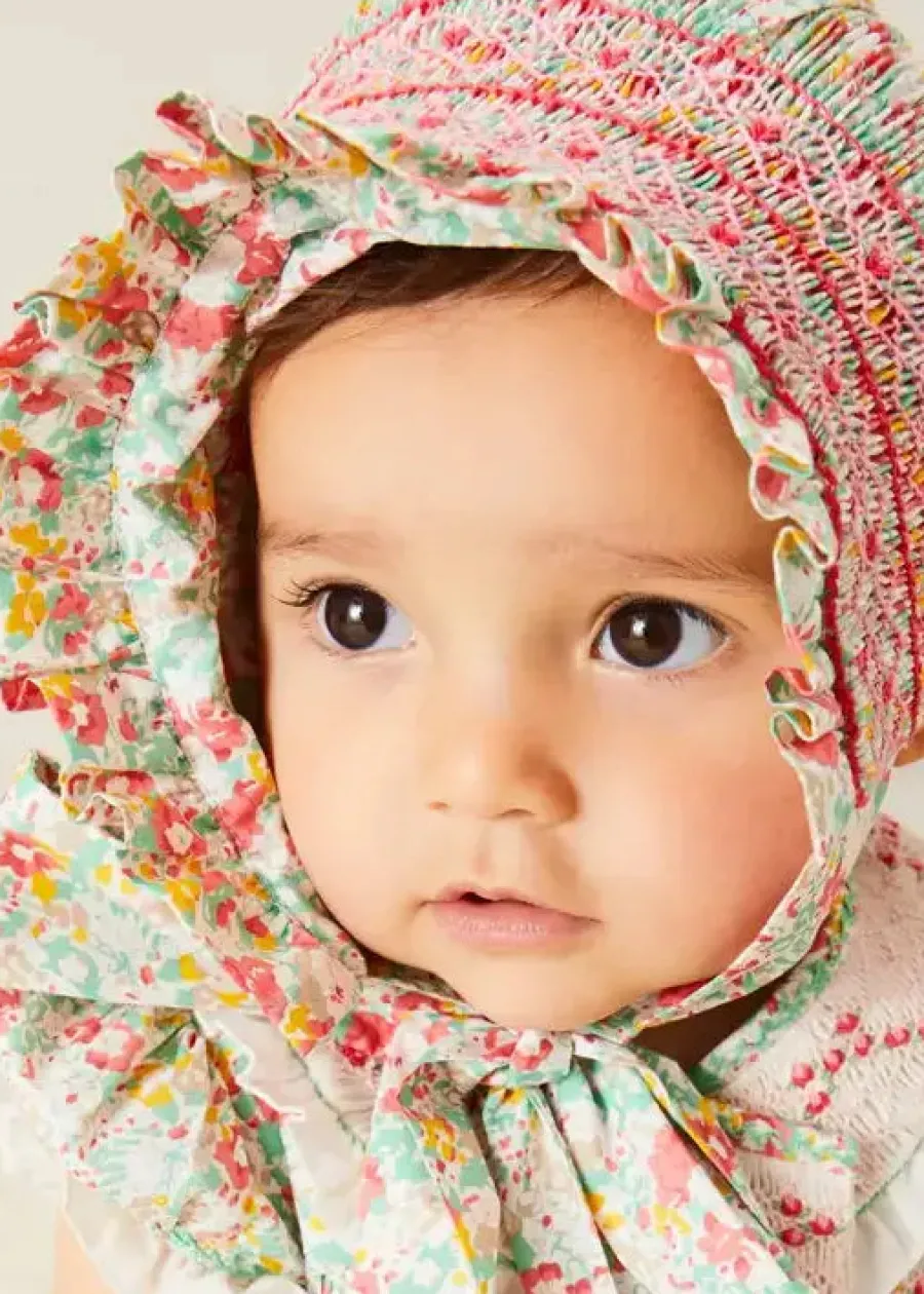 Pepa London Clementine Floral Hand Smocked Double Breasted Short Sleeve Romper in Coral (6mths-3yrs) | Clementine Floral Hand Smocked Bonnet in Coral (S-M) | Openwork Cotton Cardigan in Cream (6mths-10yrs) | Leather Mary Jane Pram Shoes in Ivory (17-20EU) | Openwork short socks White (0mths-8yrs)