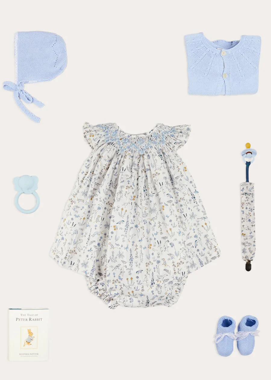 Pepa London Ellis Sleeveless Dress with Bloomer and Bows in Blue Made with Liberty Fabric (1-12m) | Openwork Detail Baby Cardigan in Blue (1-12mths) | Lace Detail Knitted Bonnet in Blue (1-6mths) | Lace Detail Knitted Booties in Blue | Ellis Dummy Clip in Blue Made with Liberty Fabric | BIBS Dummy in Blue