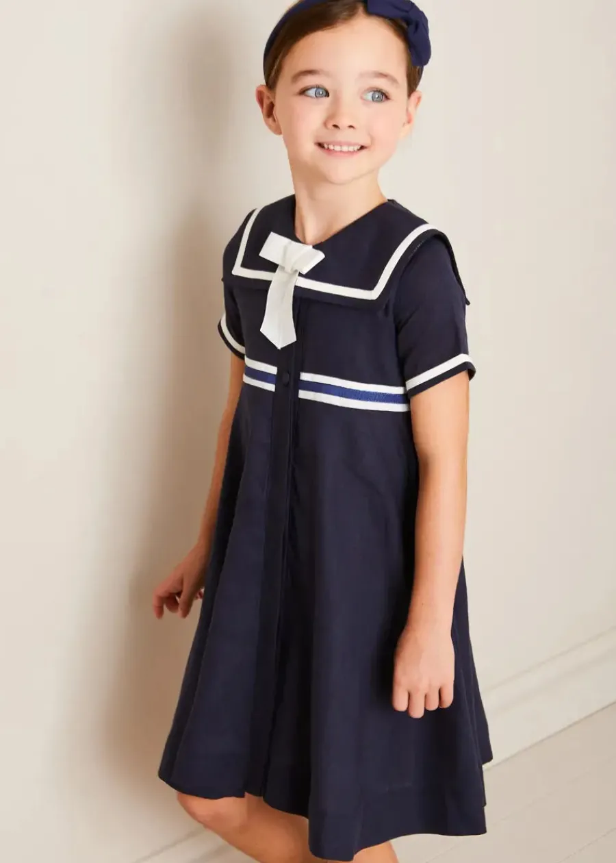 Pepa London Mariner Collar Bow Detail Short Sleeve Dress in Navy (4-12yrs) | Plain Cardigan in Navy (6mths-10yrs) | Girls Ivory Leather Mary Jane Shoes (20-34EU) | Navy Linen Big Bow Hairband | Cotton Short Socks Cream (0mths-10yrs)