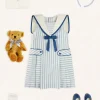 Pepa London Regency Striped Mariner Collar Pleated Sleeveless Dress in Blue (2-10yrs) | Openwork Cotton Cardigan in Cream (6mths-10yrs) | Limited Edition Merrythought & Pepa Teddy Bear With Regency Striped Bow in Blue (S-L) | Blue Linen Big Bow Hairband | Openwork short socks White (0mths-8yrs)